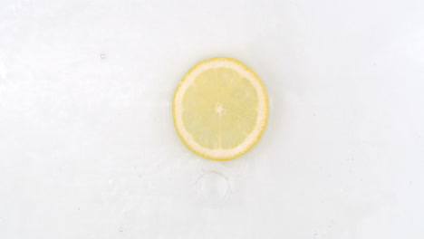 On-a-white-background-a-splash-of-water-falls-on-a-slice-of-lemon-in-slow-motion.